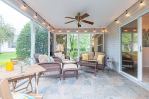 Un patio techado con mobiliario de mimbre, ventilador de techo y luces colgantes.