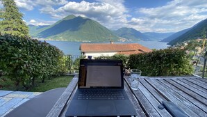 Ein Laptop auf einem Holztisch mit Blick auf einen See und Berge im Hintergrund.