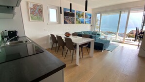 Eine moderne Küche mit Spüle und Essbereich mit Tisch und Stühlen. Ein Sofa und Meerblick durch große Fenster.