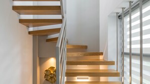 Una moderna scala con gradini in legno e ringhiere in metallo, che conduce a una piattaforma con un punto luce a parete.