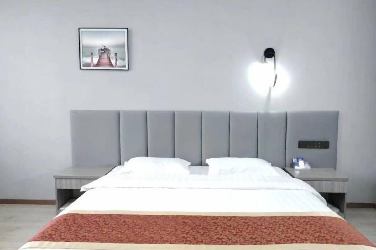 Une chambre d’hôtel avec un lit, des tables de chevet, une lampe fixée au mur et un tableau encadré.