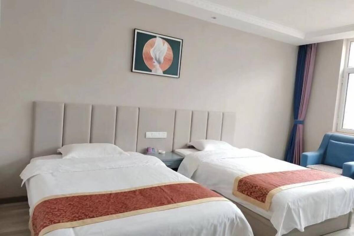 Une chambre d’hôtel avec deux lits, une tête de lit, une table de chevet, une chaise et un tableau au mur.