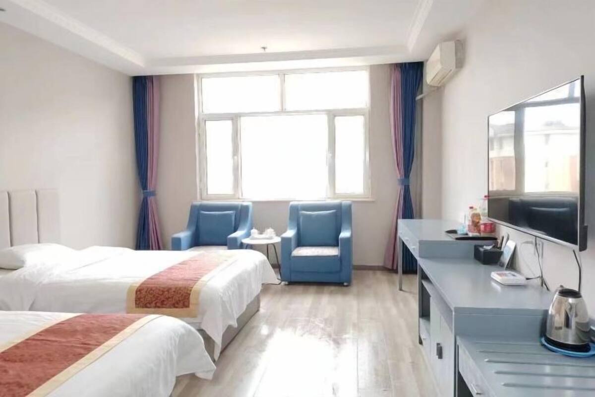 Une chambre d’hôtel avec deux lits, une télévision, un bureau avec une bouilloire et une fen être avec des rideaux.
