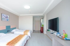 Habitación de hotel con dos camas, un televisor, un escritorio con diversos objetos y un pasillo que conduce a otra habitación.