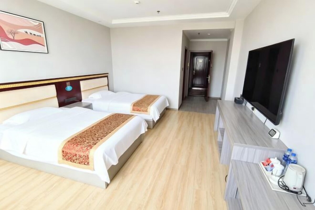 A hotel room with two beds, a TV, and a desk with a phone and water bottle.