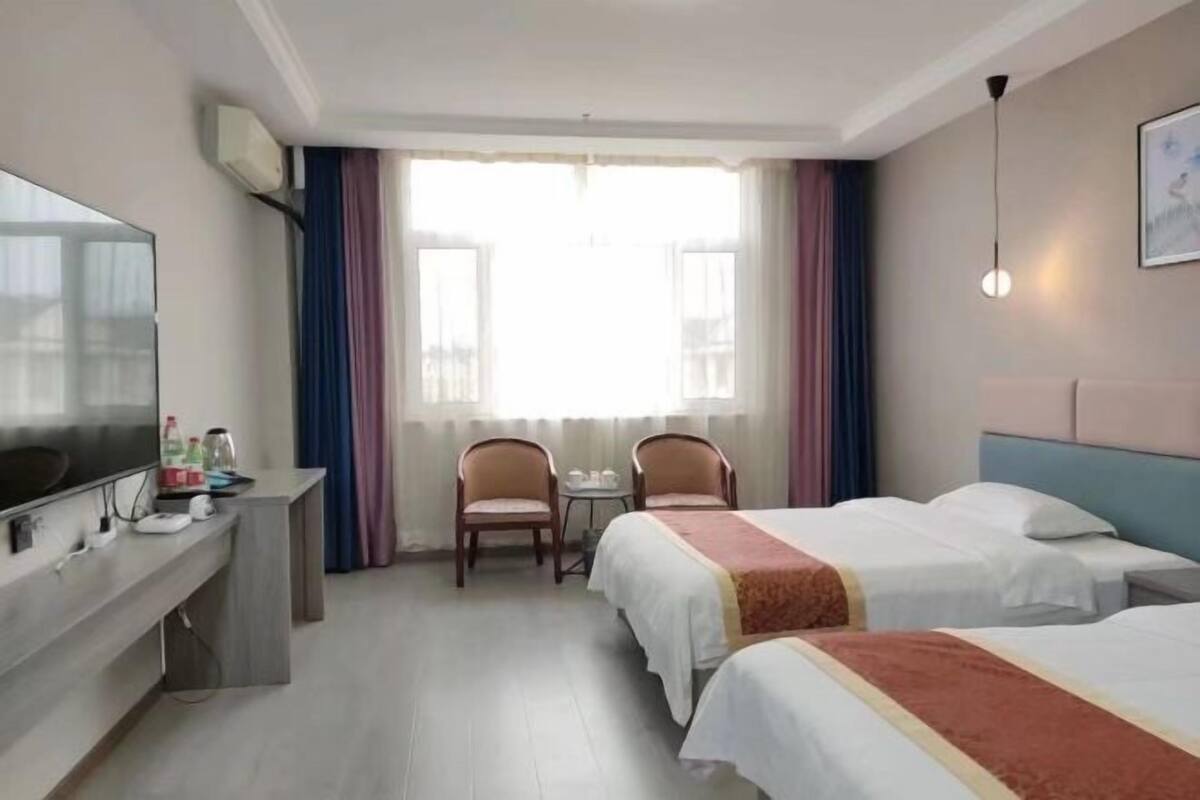 Une chambre d’hôtel avec deux lits, un bureau, une télévision et une fenêtre avec des rideaux.