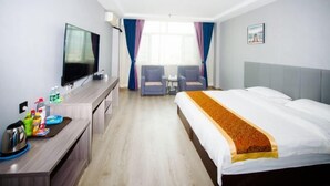 A hotel room with a bed, a desk with a TV, a small table, two chairs, and a window with curtains. - Huayi Selected Hotel (Hohhot)