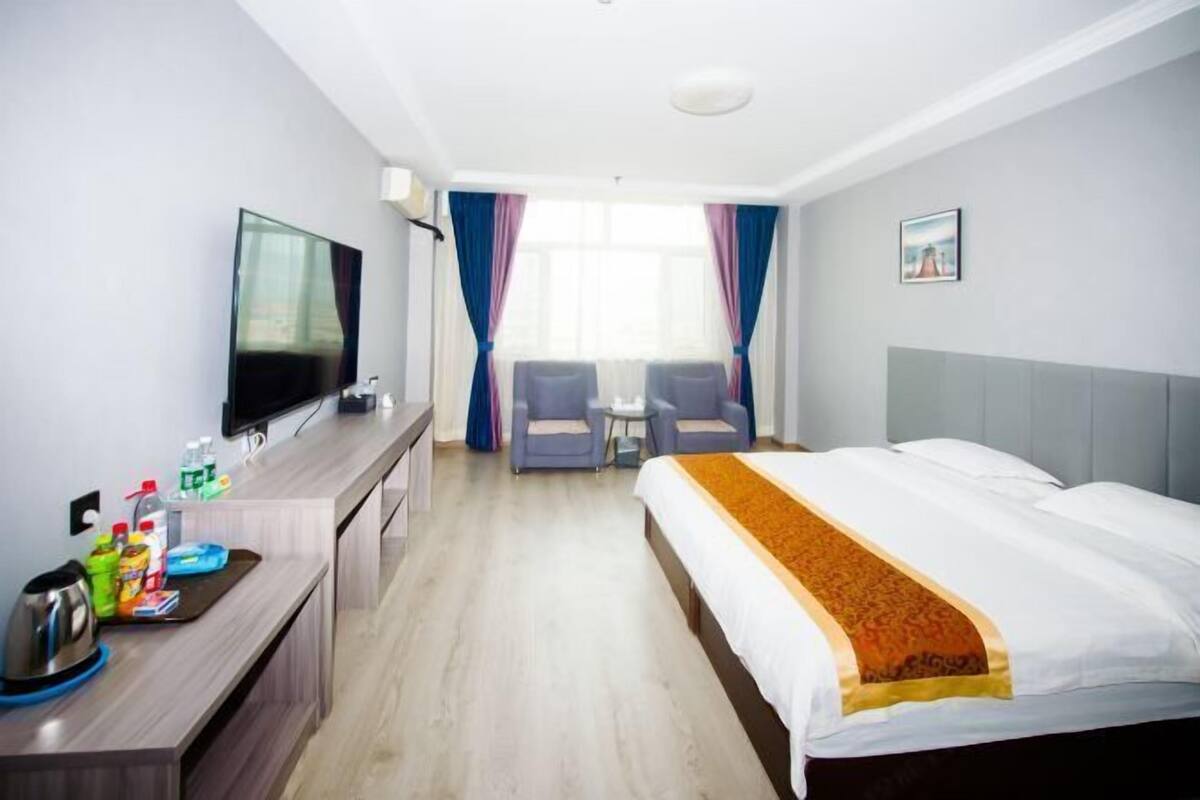 Une chambre d’hôtel comprenant un lit, un bureau avec une télévision, une petite table, deux chaises et une fenêtre avec des rideaux.