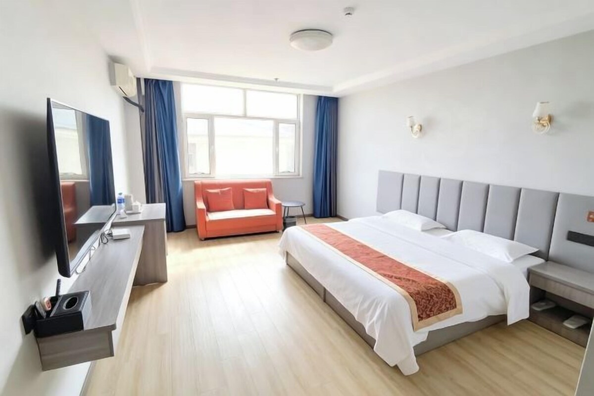 A hotel room with a bed, a TV, a desk, and a window with curtains.