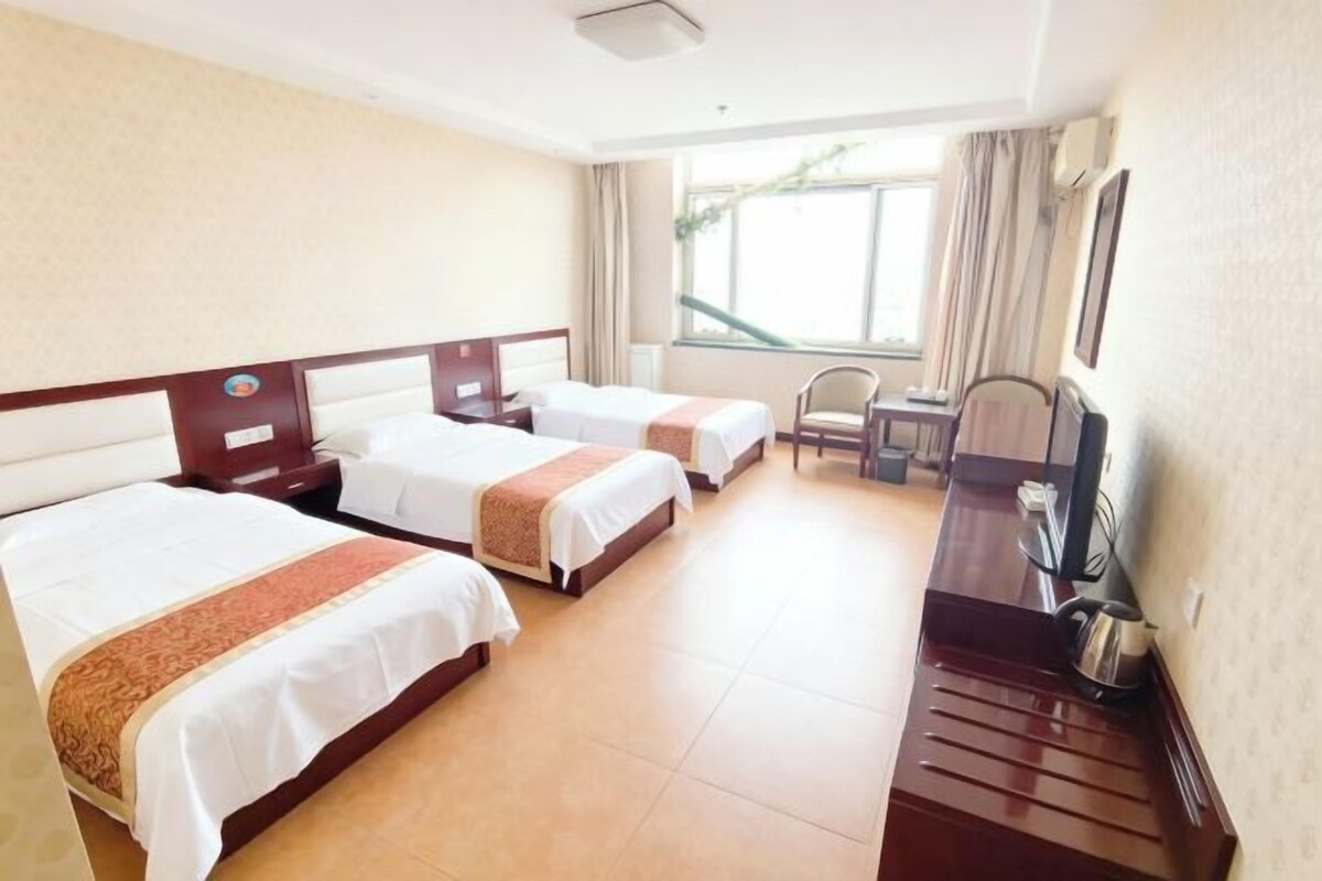 A hotel room with three beds, a desk, a chair, and a television.