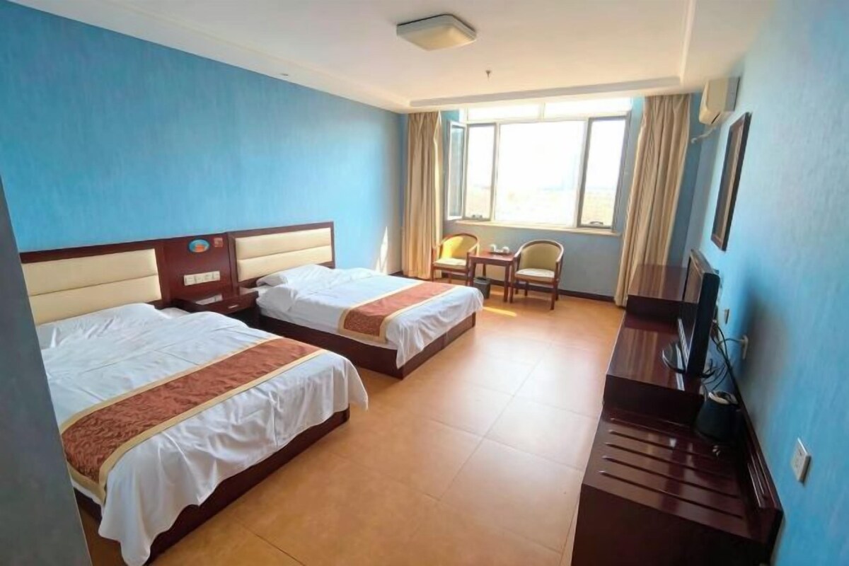 A hotel room with two beds, a desk, a chair, and a TV.
