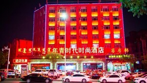 A hotel with multiple floors, brightly lit windows, and a parking lot filled with cars. - Huayi Selected Hotel (Hohhot)