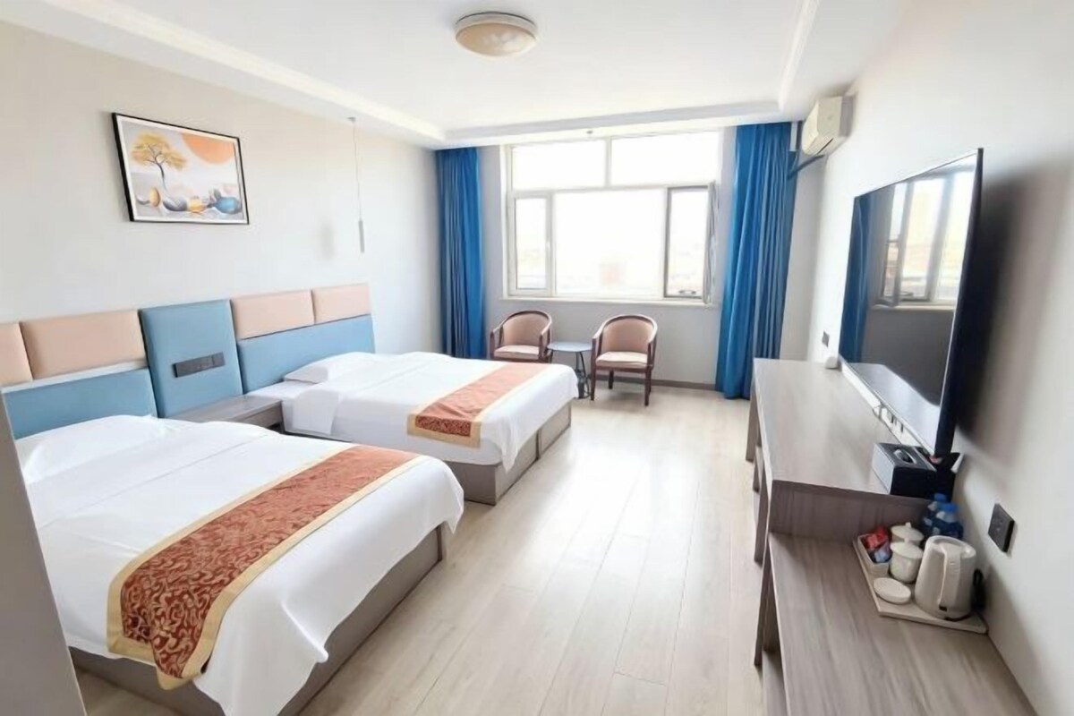 A hotel room with two beds, a desk, a chair, a TV, and a window with curtains.
