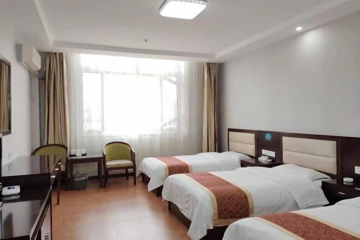 Une chambre d’hôtel avec deux lits, un bureau, une chaise, une petite table et une fenêtre avec des rideaux.