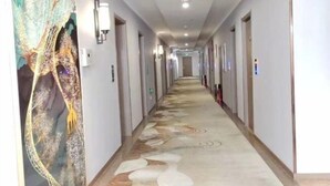 A long, narrow hallway with patterned carpet, light-colored walls, and doors on either side. - Huayi Selected Hotel (Hohhot)
