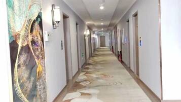 A hotel corridor with a patterned carpet, doors on both sides, and wall-mounted light fixtures.
