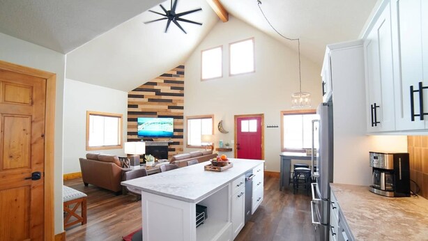 A spacious living area with a large TV, a fireplace, and a kitchen with a refrigerator and coffee maker. - Mountain Modern Family Home near Grand Targhee - Hot Tub (Driggs)
