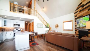A spacious living area with a wooden staircase, a kitchen with white cabinets, and a fireplace. - Mountain Modern Family Home near Grand Targhee - Hot Tub (Driggs)