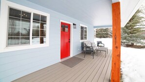 A covered porch with a red door, two windows, and a wooden deck. - Mountain Modern Family Home near Grand Targhee - Hot Tub (Driggs)