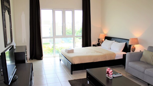 A hotel room with a bed, a sofa, a TV, and a window with curtains. - KSLV - Furnished Studio (Dubai)