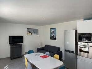 Um espaço de estar moderno e compacto, com televisão de tela plana, sofá, mesa de jantar e forno embutido e micro-ondas.