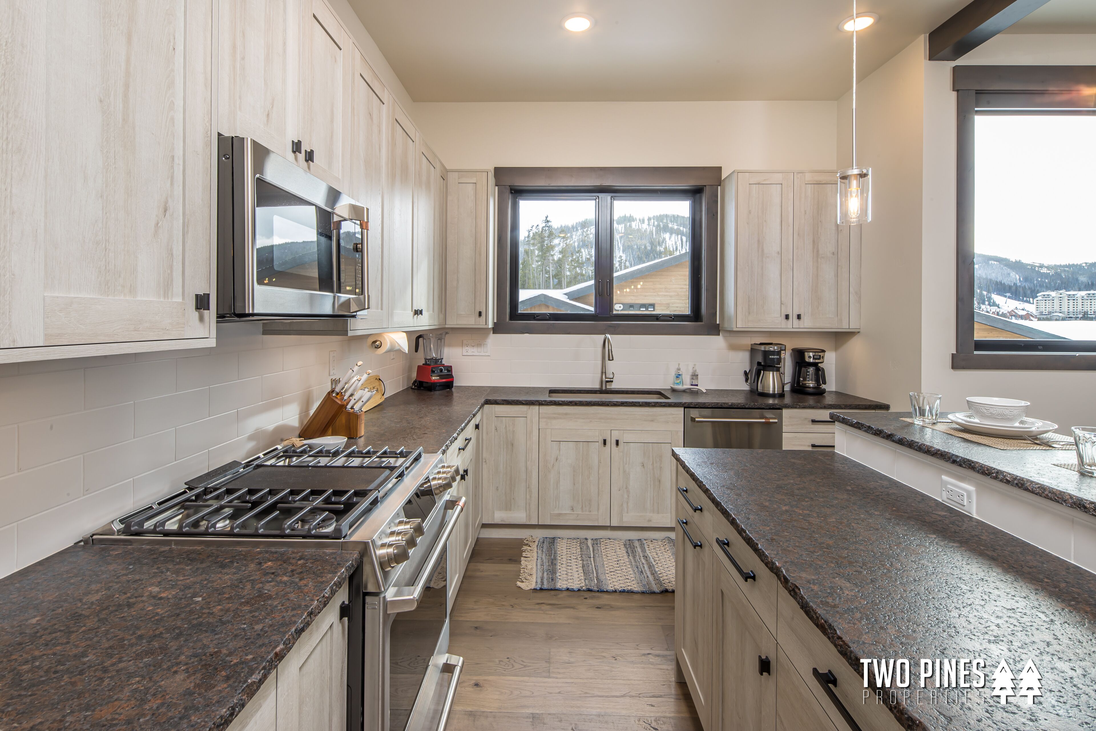 A modern kitchen with granite countertops, stainless steel appliances, and a large window offering a view of a snowy landscape.