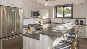 Une cuisine moderne dotée d’appareils électroménagers en acier inoxydable, d’un grand îlot central avec des tabourets de bar et d’une vue sur l’extérieur grâce à une fenêtre.