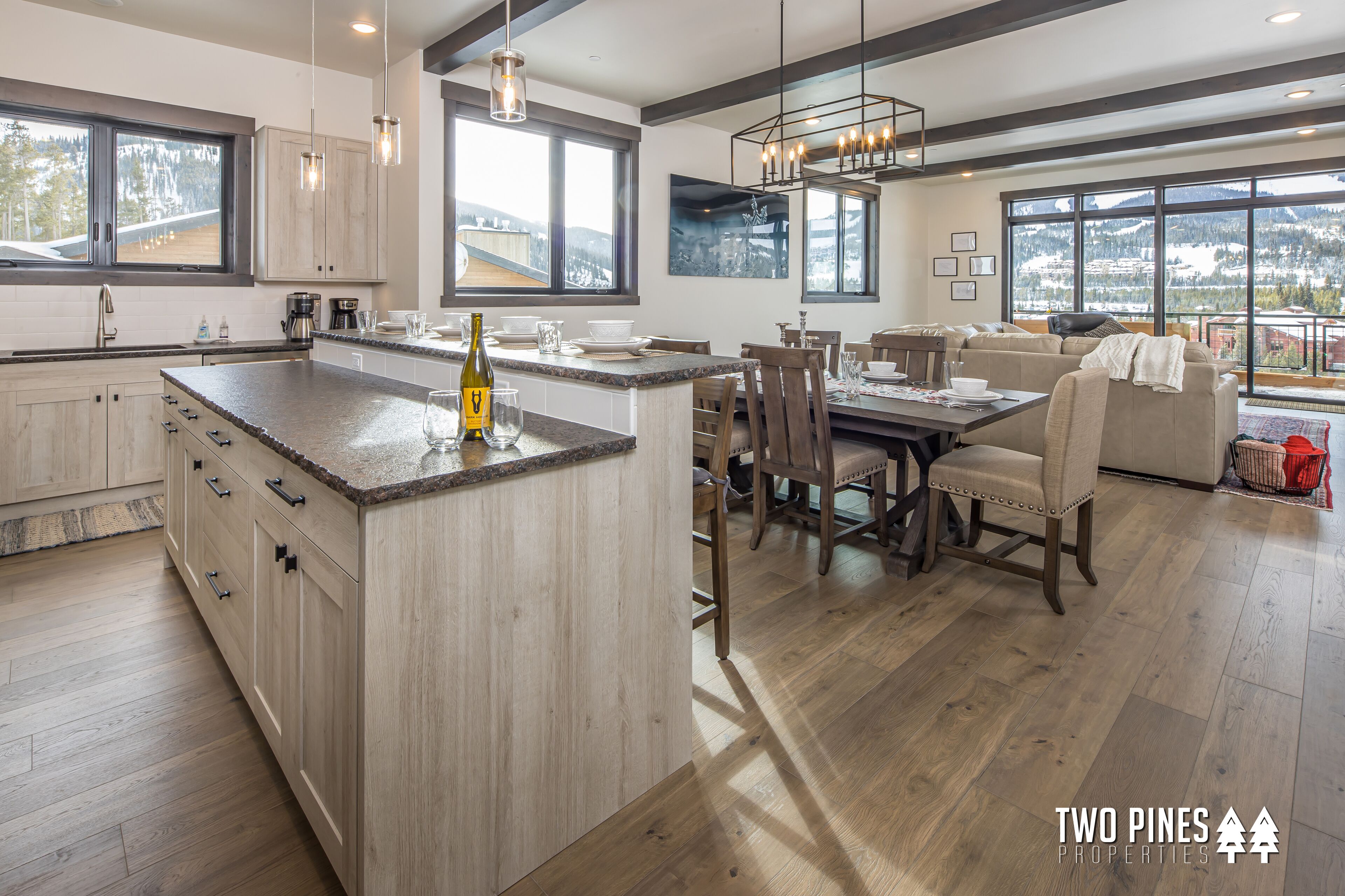 A modern kitchen with a large island, wooden cabinets, and a dining area with a view of the mountains.