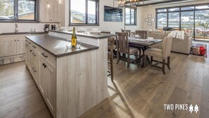 Une cuisine moderne dotée d’un grand îlot central, de meubles en bois et d’un coin repas offrant une vue sur les montagnes.