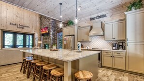 Une cuisine moderne dotée d’un grand îlot central, de tabourets de bar, d’éléments décoratifs en bois et d’un mur d’accent en pierre.