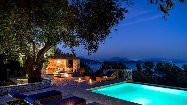 An outdoor pool area with lounge chairs, a stone wall, and a small seating area under a tree.