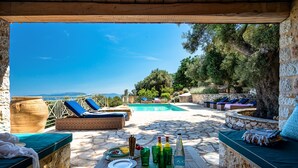 A poolside area with lounge chairs, a stone table with plates and bottles, and a view of the sea.