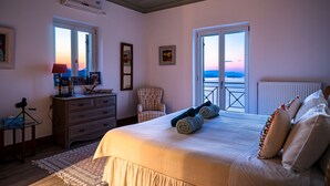 A bedroom with a large bed, a dresser, a chair, and a view of the outside.