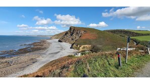 Un paysage côtier avec une plage rocheuse, une falaise et une colline herbeuse.