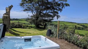 Un bain à remous dans un jardin offrant une vue sur des collines verdoyantes et un grand arbre.