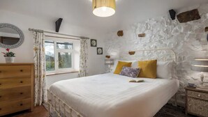 Une chambre à coucher avec un lit, une commode en bois et un mur en pierre.