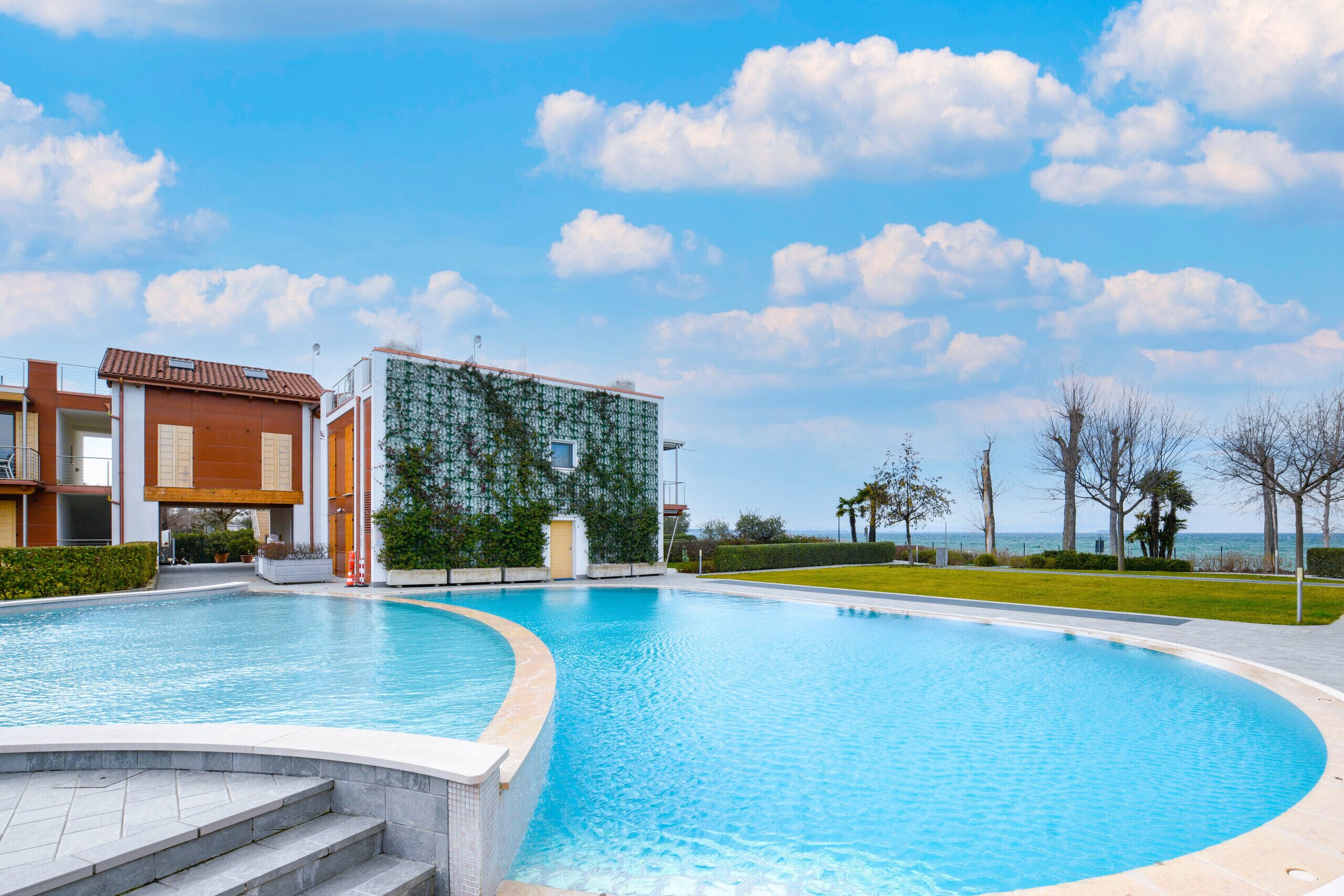 Ein Pool mit geschwungener Kante neben einem Gebäude mit einem Ziegeldach und einer grünen Wand.