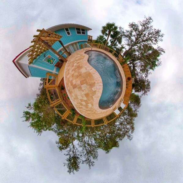 Una piscina circular con cubierta de madera, un edificio azul con ventanas y árboles al fondo.
