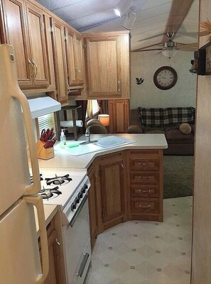 Compact kitchen with a refrigerator, stove, sink, and clock.