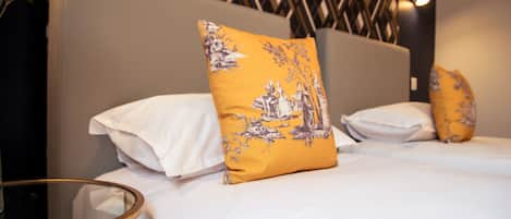 A neatly made bed with white linens and a single yellow pillow with a floral design.