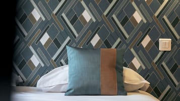A hotel room with a patterned wall, a bed with pillows, and a wall-mounted light.