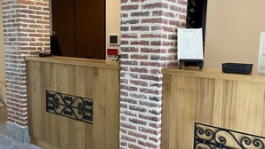 A reception area with a brick wall, wooden reception desk, and a tiled floor. -  Le Petit Perier (Laval)