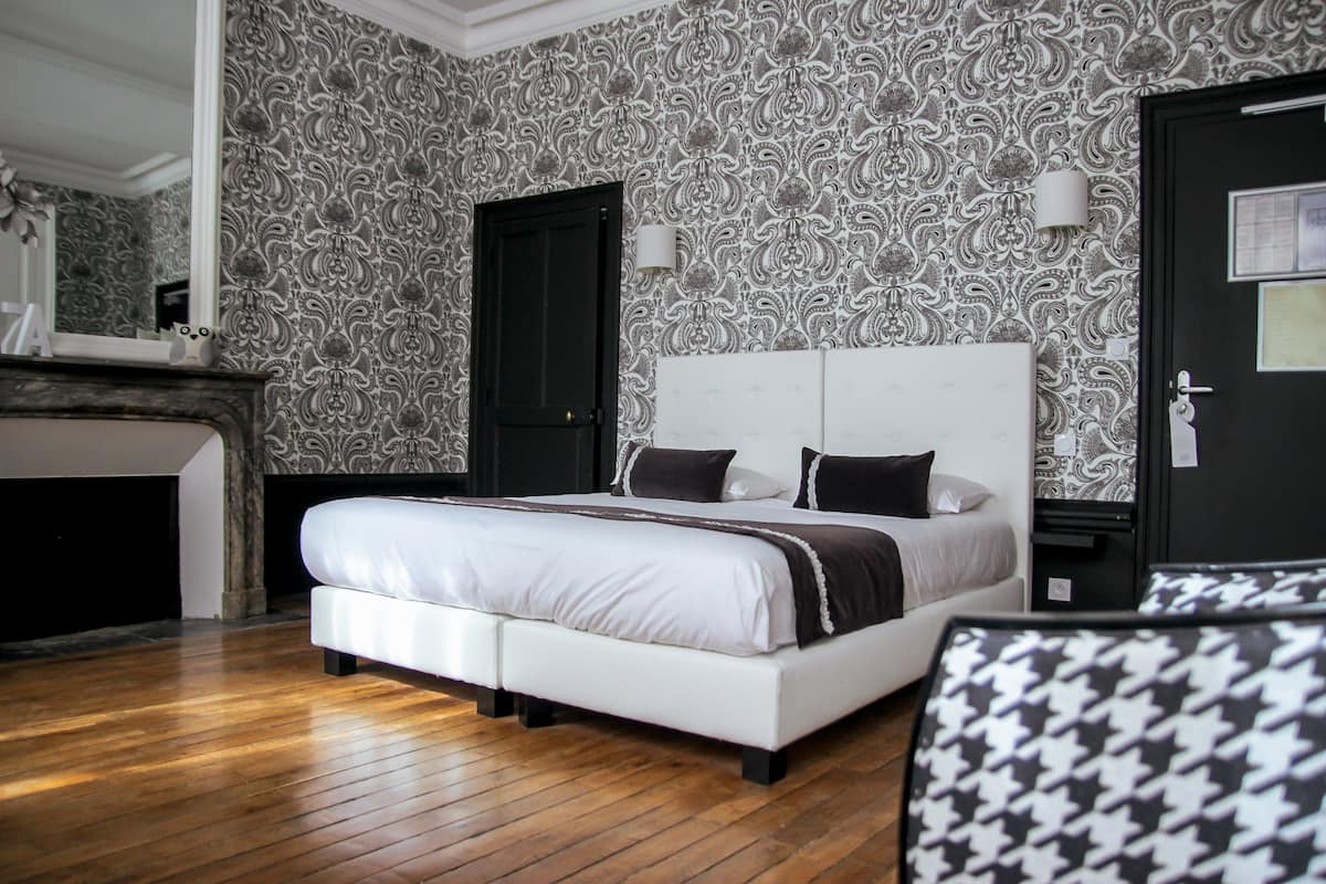Quarto com uma cama grande, lareira, papel de parede estampado e uma porta preta.
