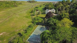 Una cancha de tenis rodeada de exuberante vegetación y una casa grande con vistas al mar.