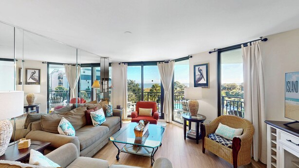A spacious living room with a sofa, armchairs, a glass coffee table, and a balcony with a view of the sea. - Shipwatch C317: Oceanfront Escape in Wild Dunes – Your Cozy Island Retreat (Isle Of Palms)
