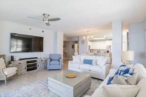 A spacious living room with a flat-screen TV, a sofa, a coffee table, and a ceiling fan.