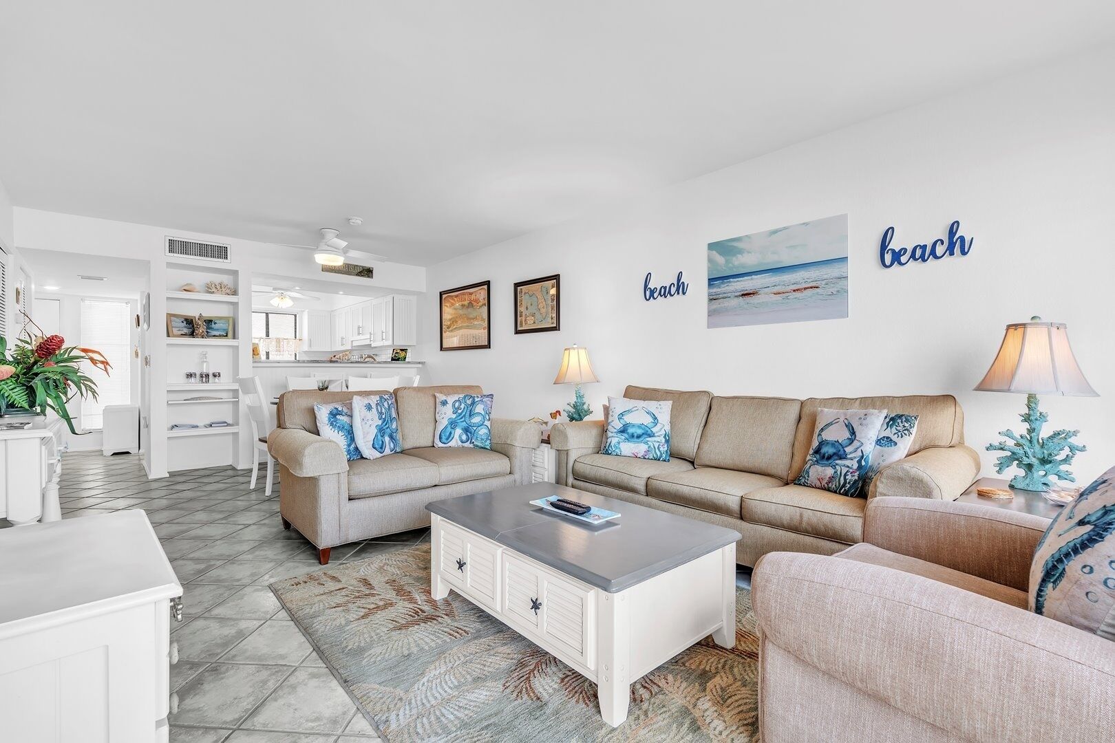 Una sala moderna con un sofá beige, una mesa de centro blanca y una zona de comedor con armarios blancos.