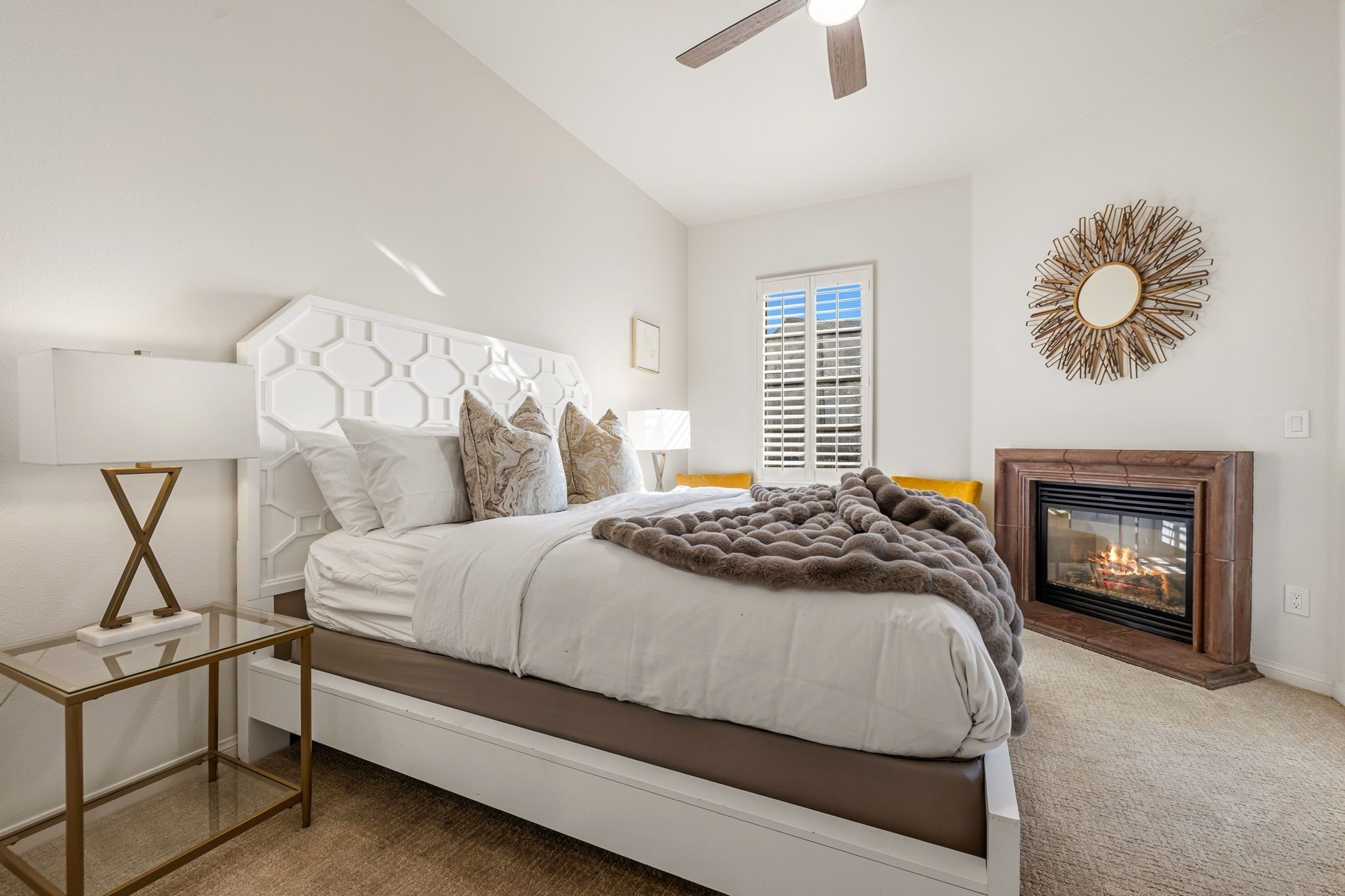 Une chambre à coucher avec un lit, une cheminée, un ventilateur de plafond et une fenêtre avec des stores.
