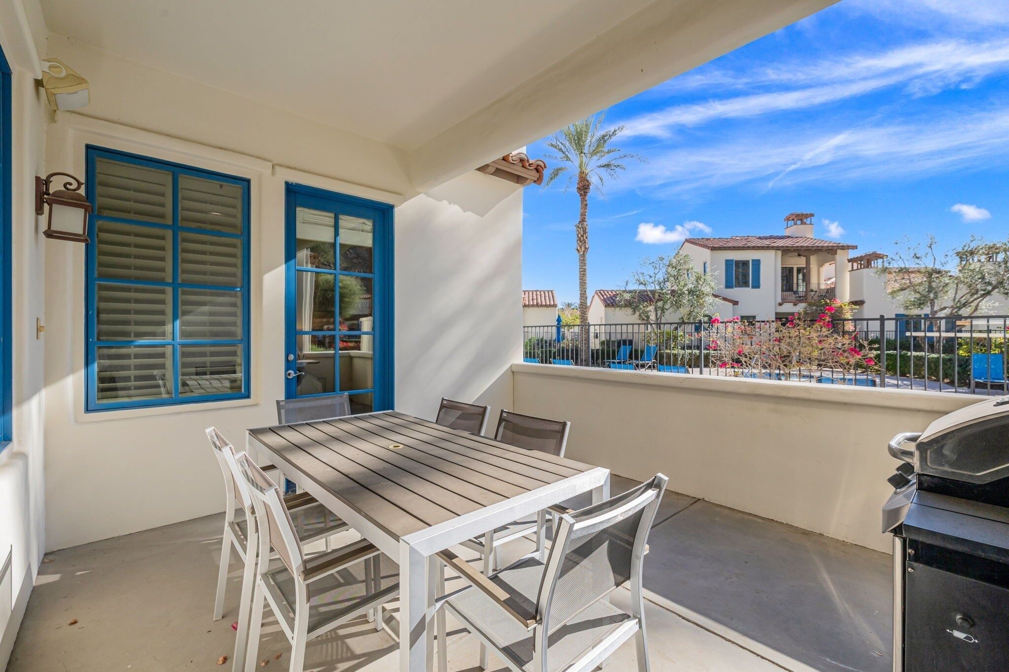 A balcony with a table and chairs, a grill, and a view of neighboring houses.