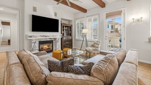 A living room with a fireplace, a large TV, and a ceiling fan. - Luxurious 2 Story Townhome - Newly Remodeled! 3 Bedroom Condo by RedAwning (La Quinta)
